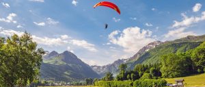 Un parapentiste en plein vol au-dessus de Val Louron - Loudenvielle, entouré de montagnes verdoyantes et d'un ciel bleu parsemé de nuages.